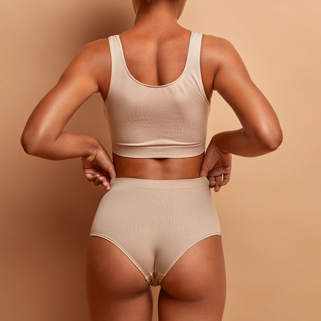 Back view of sensual slim woman poses in panties and top has perfect figure healthy dark skin isolated on brown background.