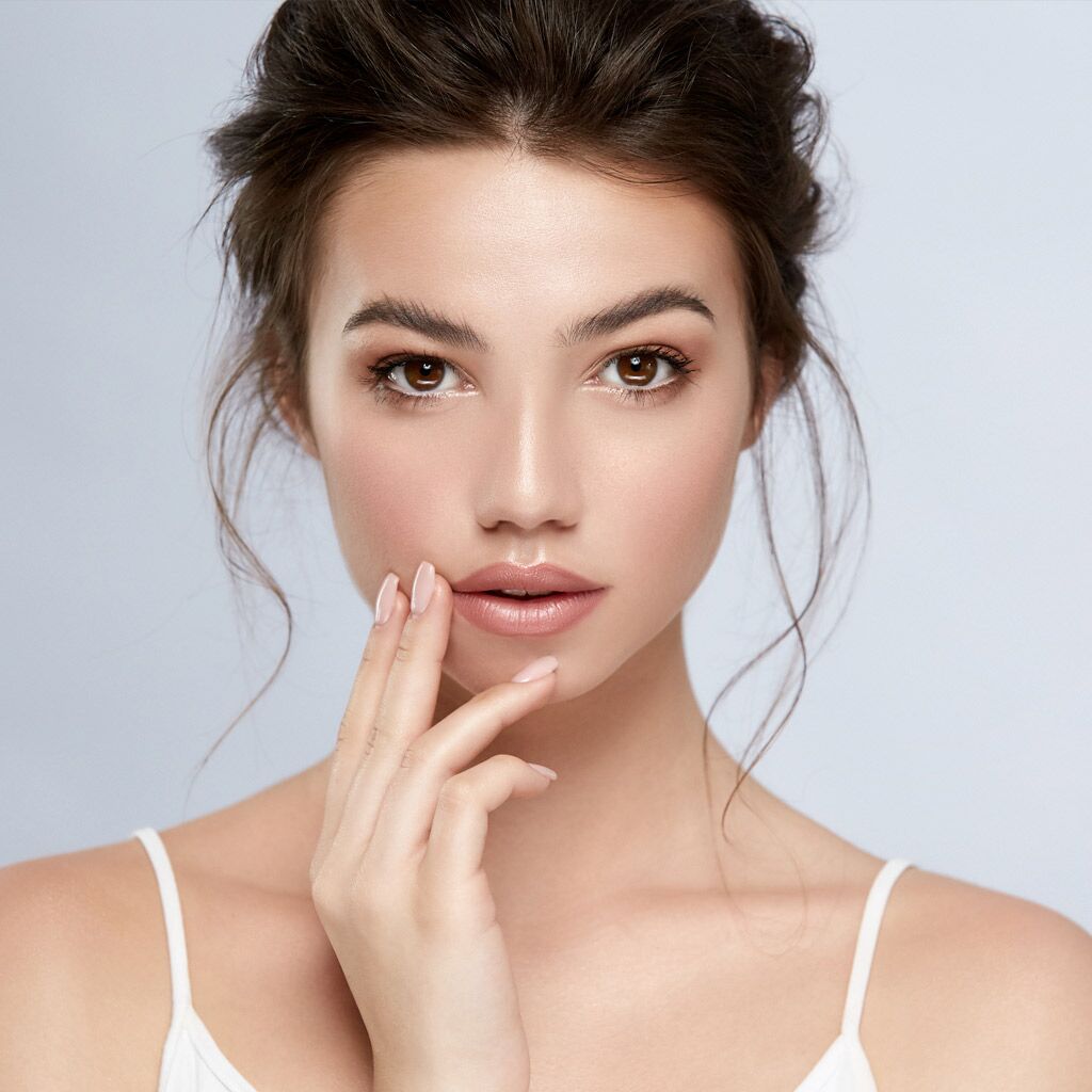 sexy model with perfect skin and dark eyes looking to camera and touching face with arm