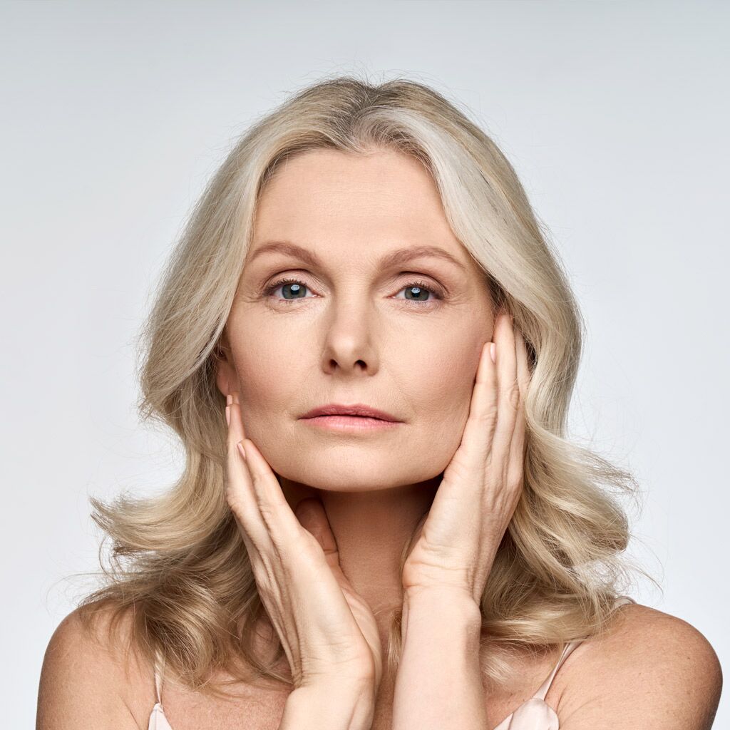 Adult senior older woman touching her perfect skin. Beautiful portrait mid 50s aged woman advertising facial anti age lift products salon care tighten skin isolated on white looking at camera