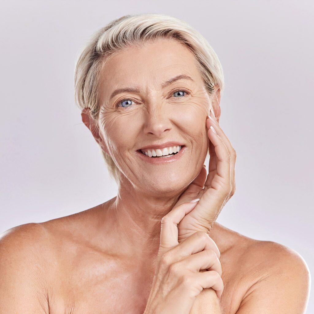 Portrait of happy smiling mature caucasian woman looking positive and cheerful against studio background. Smooth face and skin of an older female or antiaging beauty model doing her skincare routine